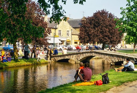 Menschen am Flussufer sitzend, River Windrush, Bourton on the Water, Gloucestershire, England, UK