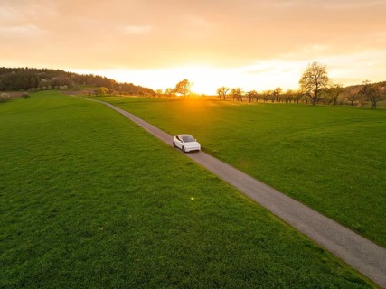 A car drives on a long road through a green landscape at sunset, Tesla New Model Y, Germany