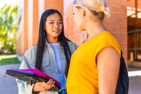 Two multi-ethnic female friends talking outside the university entrance