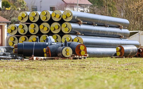 Stacked district heating pipes and district heating pipes with yellow ends are stacked in a meadow