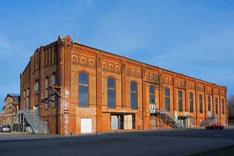 Large, old brick factory building with large windows under a clear sky, blowing hall, Ilseder