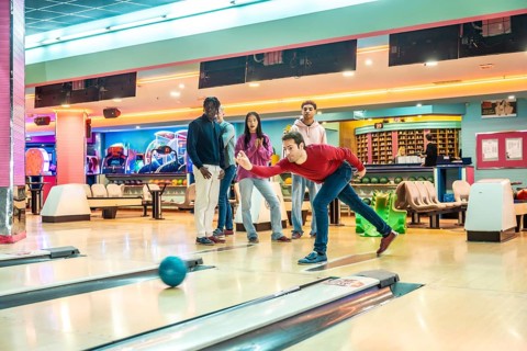 Group of multi ethnic friends playing bowling together, having fun on the weekend in a brightly lit