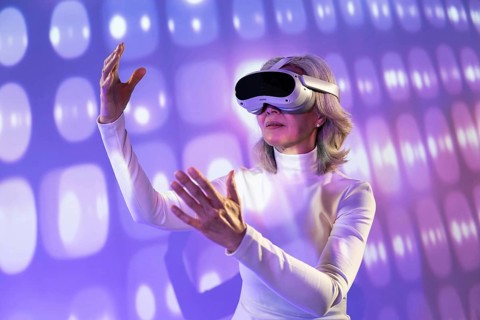 An elderly Asian woman is immersed in the metaverse, wearing virtual reality goggles. She stands in