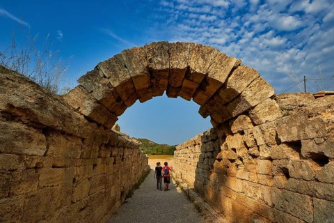 Crypt, vaulted corridor to the stadium, two people walk through an old stone arch wall under a