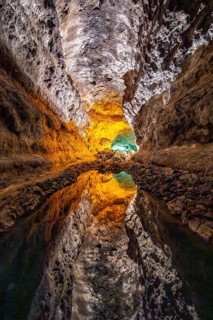 Lava tunnel, illuminated lava cave with perfect reflection in an underground lake, Cueva de los