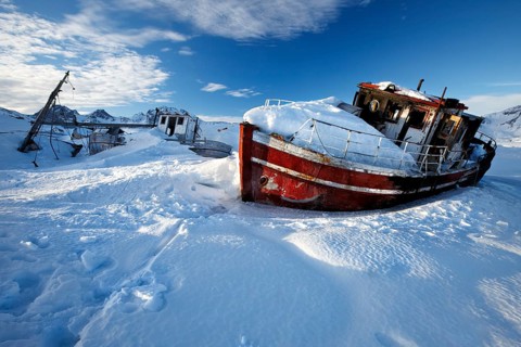 Kong Oscar Havn. Tasiilaq, East Greenland – a fishing boats lies frozen in the harbor, trapped by