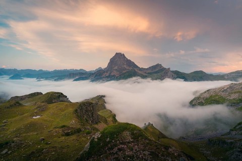 A stunning view of a mountain peak emerging above thick clouds, bathed in the warm hues of a