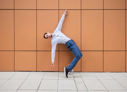 A Cuban male dancer leans artistically against a brown tiled wall, showcasing his dance skills. He