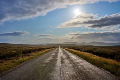 Sun rays penetrate the clouds over a long road that crosses a vast landscape, Tongue, Lairg,