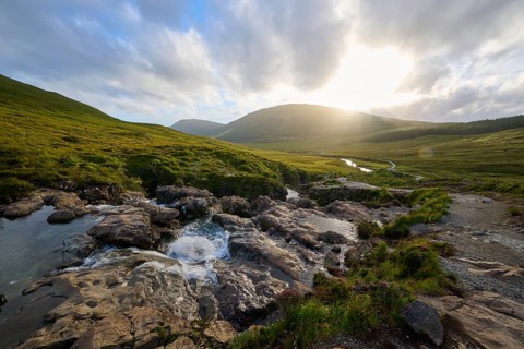River flows through green hills in sunset light under a cloudy sky, Fairy Pools, Grula, Isle of