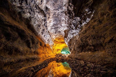Lava tunnel, illuminated lava cave with perfect reflection in an underground lake, Cueva de los