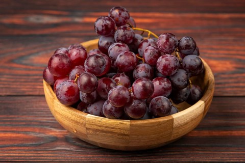 Fresh grapes in a wooden bowl on a dark wooden background