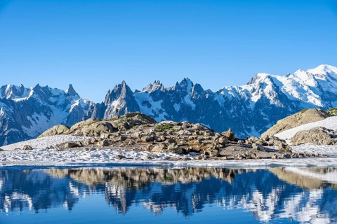 Young man in front of impressive mountain landscape in morning light, reflection in the Lac Blanc