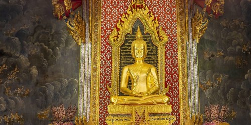 Golden meditating Buddha surrounded by wall paintings with Buddhist teachings and representations