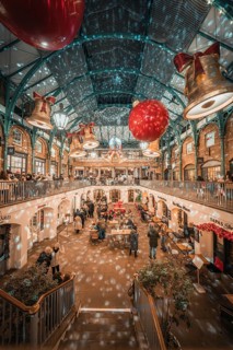 People in a festively decorated market hall with twinkling lights and Christmas decorations,