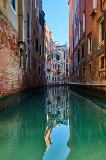 View from a gondola on a waterway in Venice going through the houses on a quiet and sunny morning