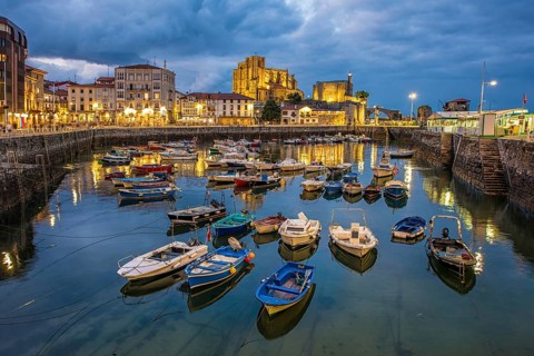 Tranquil evening view of a Castro Urdiales marina, showcasing colorful boats reflected in the calm