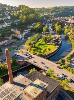 Aerial view of a bridge over a canal in a green town with surrounding houses and hilly landscape,