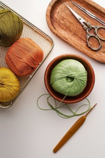 Top view of a needlework setup showcasing colorful yarns in baskets and bowls, vintage scissors,