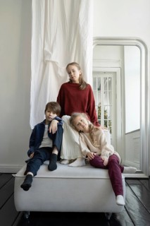 Three children dressed in casual, cozy attire pose together in a bright, minimalistic room The calm
