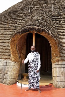 Rwandan man, 25 years old, wearing traditional dress at the entrance to the Royal Palace replica in
