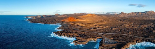 Coast with lava fields, volcanic landscape near Los Hervideros with red volcano Montaña Bermeja, in