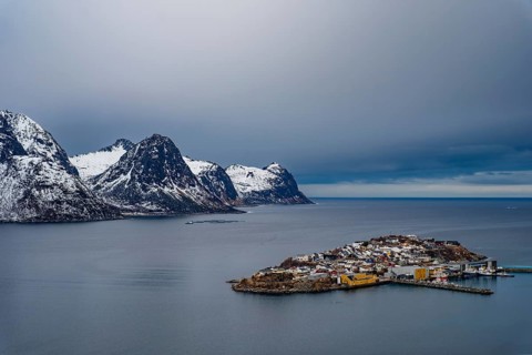 Husøy island in the fjord, snow-capped mountains behind it, Senja island, Troms, Norway
