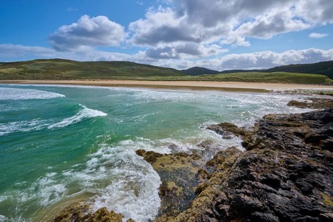 Coastal landscape with waves, rocks and sandy beach under blue sky with clouds, Farr Bay,