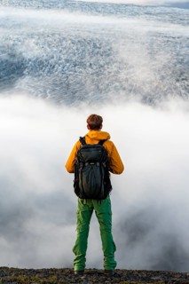 Young man in front of impressive landscape at sunset, fog, clouds moving around, glacier ice of the