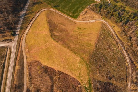 Aerial view of a hill with barren and vegetated areas, surrounded by roads, old deposit in front of