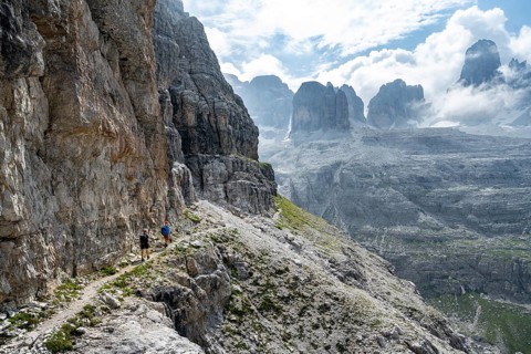 Two mountaineers on a hiking trail in front of a picturesque mountain landscape with rocky peaks,