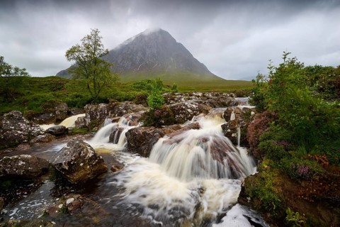 Serene water landscape with stylish waterfalls and an imposing, cloud-covered mountain in the