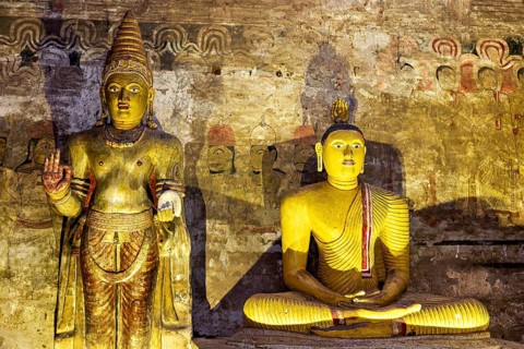 Two Buddha statues, partly in shade, in front of a painted wall, The cave temple of Dambulla in Sri