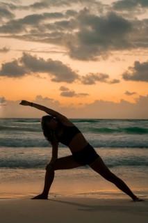 A woman performs a yoga pose on a serene beach at sunrise, surrounded by gentle waves and a vibrant