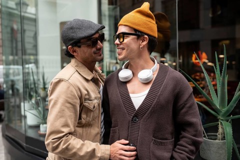 A stylish gay couple enjoys a moment together on a city street. They are smiling warmly at each