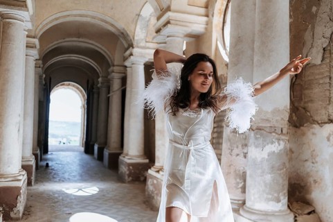 A bride wearing a delicate gown stands gracefully under the arches of an ancient villa in Treia,