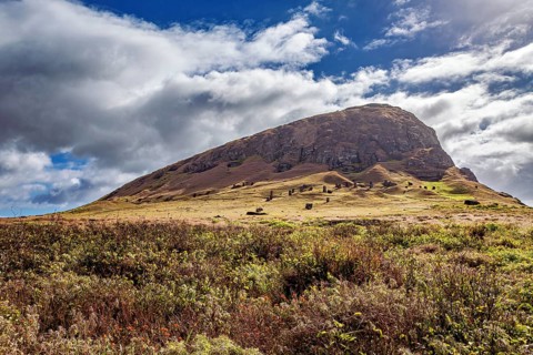 Green hill with cloudy sky and ancient rock formations, the landscape of Easter Island in the