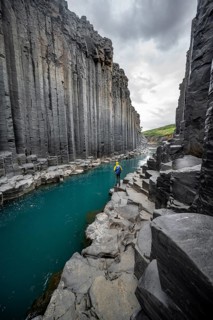 Tourist standing by the river in Stuðlagil Canyon, turquoise blue river between basalt columns,