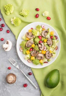 Vegetarian salad from romanesco cabbage, champignons, cranberry, avocado and pumpkin on a gray