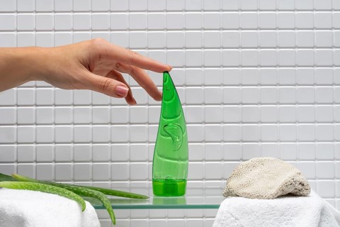 A woman's hand reaching for a bottle of aloe gel next to body care cream in a clean bathroom