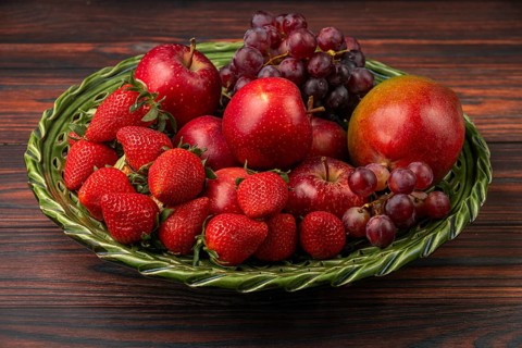 Strawberries, apples, grapes and mango in a green bowl on wood