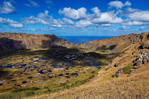 Crater with deep shadows and sweeping views over rocky landscapes to blue skies, the Ranu Kau