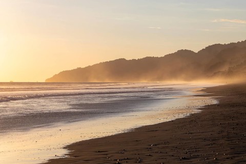 The low sun's golden light illuminates the ocean spray on Carate Beach, with views of Corcovado NP