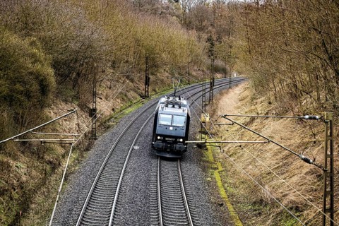 A train runs through a railway line lined with trees and shrubs in spring, electric locomotive on