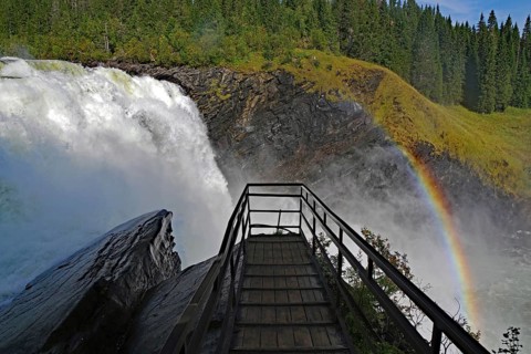 Wooden bridge leads to an impressive waterfall with rainbow in the background, Tännforsen,