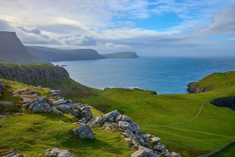 Rocky coast with green hills under a cloudy blue sky, Waterstein Head, Waterstein, Isle of Skye,