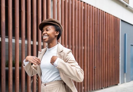 A black woman in a beige outfit and cap walks confidently in an urban environment The setting