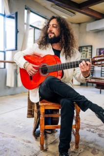 Latin man with long hair playing red bass guitar in studio