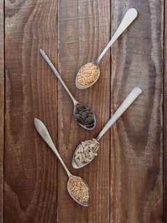 Spoons holding flax, pumpkin, sunflower, and sesame seeds on rustic wood background