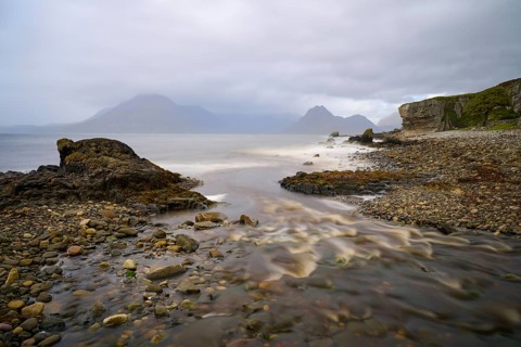 River flows into the sea along a rocky coast under grey skies, Elgol Beach, Elgol, Isle of Skye,